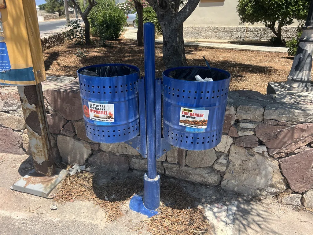 Greek and English fire awareness stickers on two blue public bins