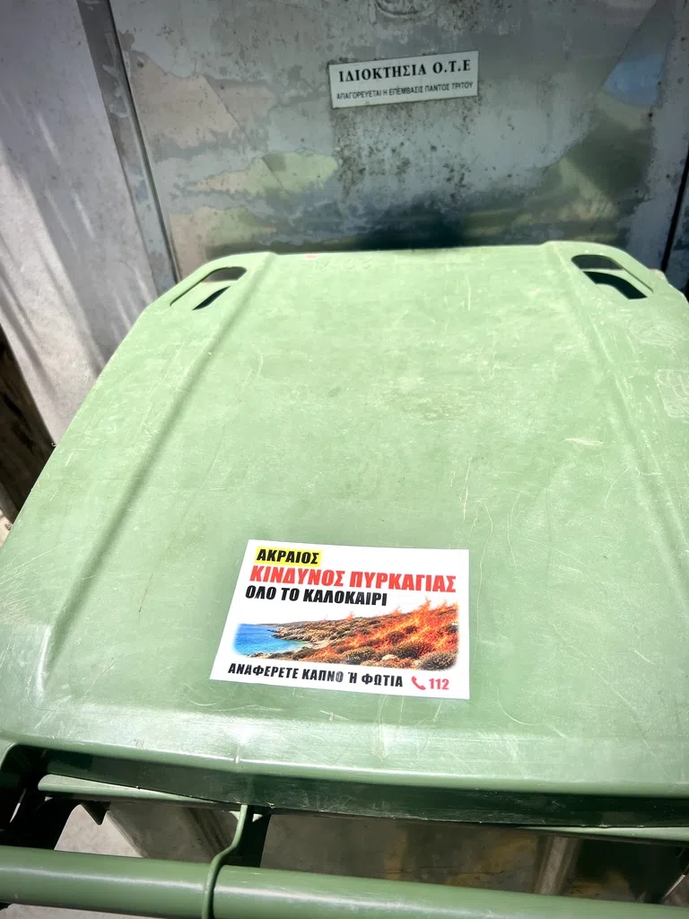 A Greek extreme fire danger sticker on the lid of a green bin